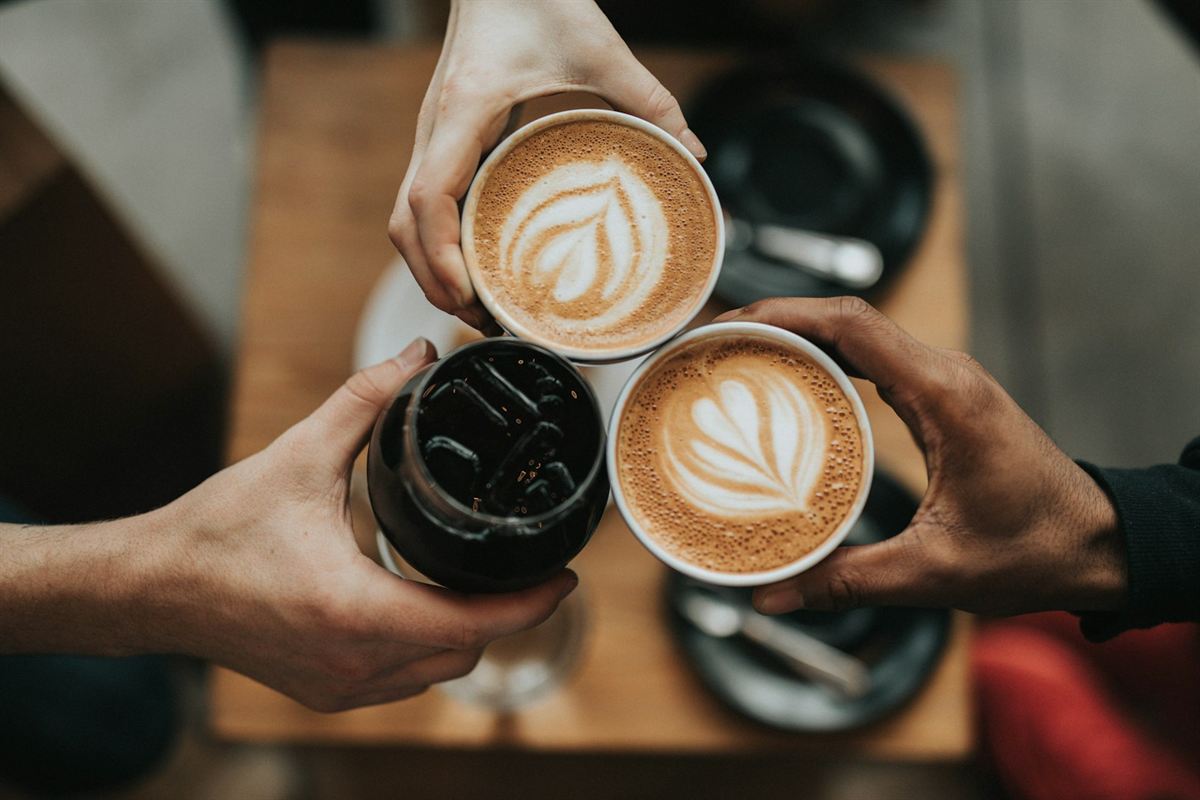 Vier Hände stoßen mit Kaffeetassen an — Kaffee und Gemeinschaft im MoccaGino Köln